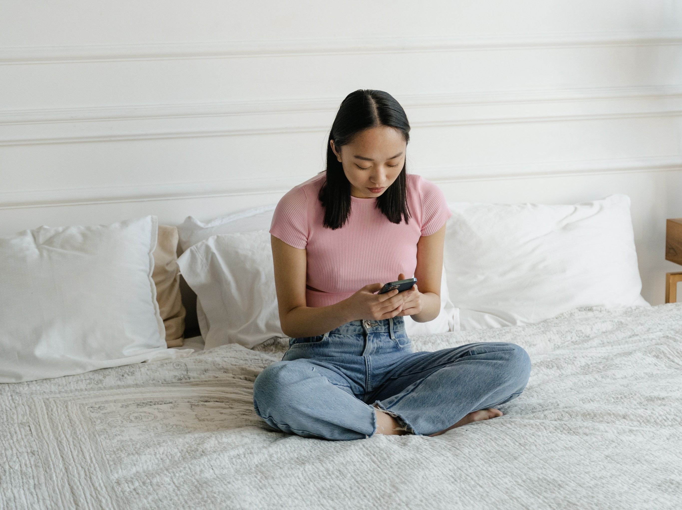 A young person sitting on their bed, on their phone